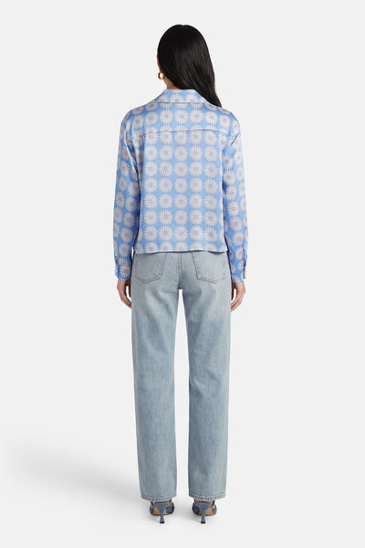 Chemise bleue à manches longues de Terra di Siena, à motif marguerite, portée avec un jean taille haute.