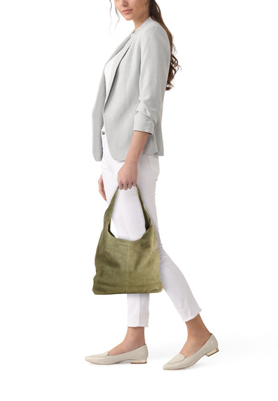 Olive green suede shoulder bag, side view, worn by model in white pants and light gray blazer, beige loafers, lifestyle shot