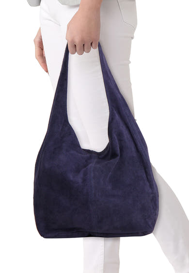 Navy blue suede shoulder bag with soft texture and slouchy design, worn by model in white pants, front view.