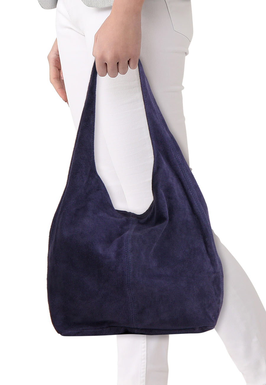 Navy blue suede shoulder bag with soft texture and slouchy design, worn by model in white pants, front view.