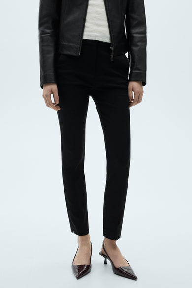 Zwarte close-fitting broek van MANGO, met gesneden zoomen en gedragen met een lederen jas en crocodilprintescarpins.
