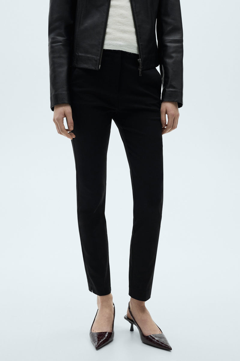 Zwarte close-fitting broek van MANGO, met gesneden zoomen en gedragen met een lederen jas en crocodilprintescarpins.