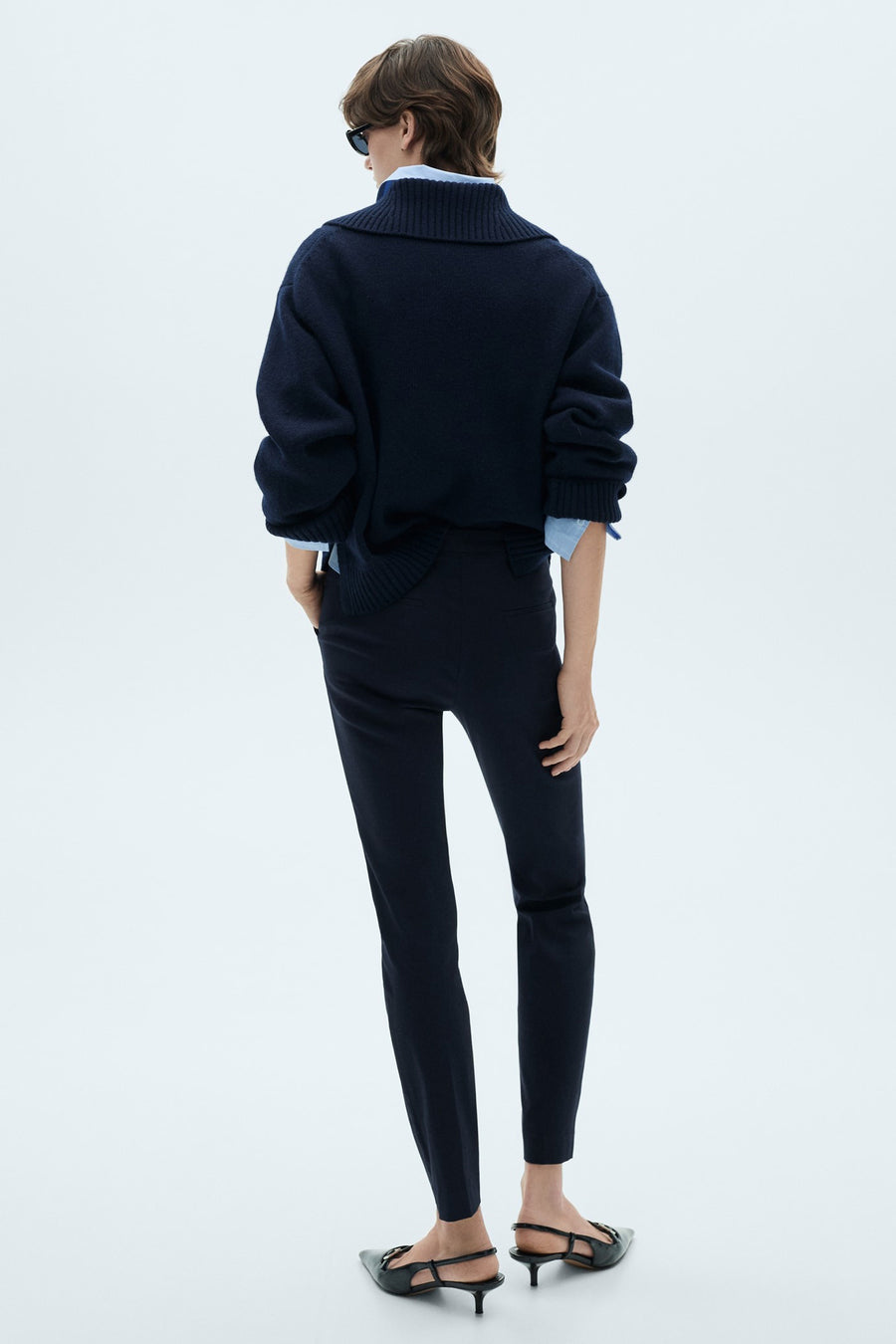 Pantalon bleu foncé de MANGO, coupe slim, porté avec un pull en maille et des chaussures à talons aiguilles.