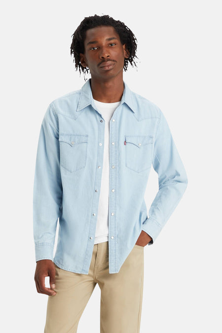 Chemise en denim bleu clair à manches longues de Levi's, portée sur un t-shirt blanc et un pantalon beige.