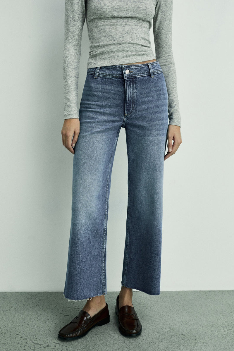 Donkerblauwe wijde jeans van MANGO, gedragen met een grijze top met lange mouwen en bruine loafers.