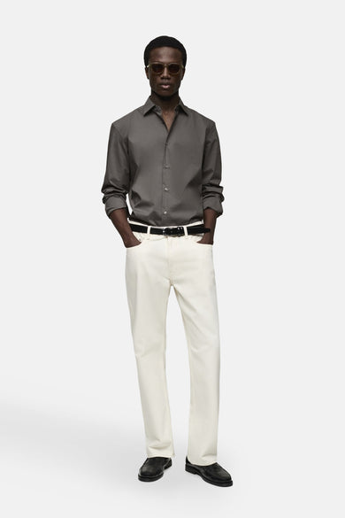 Grijze blouse met lange mouwen van MANGO, gedragen met een lichte broek, een zwarte leren riem en een zonnebril.