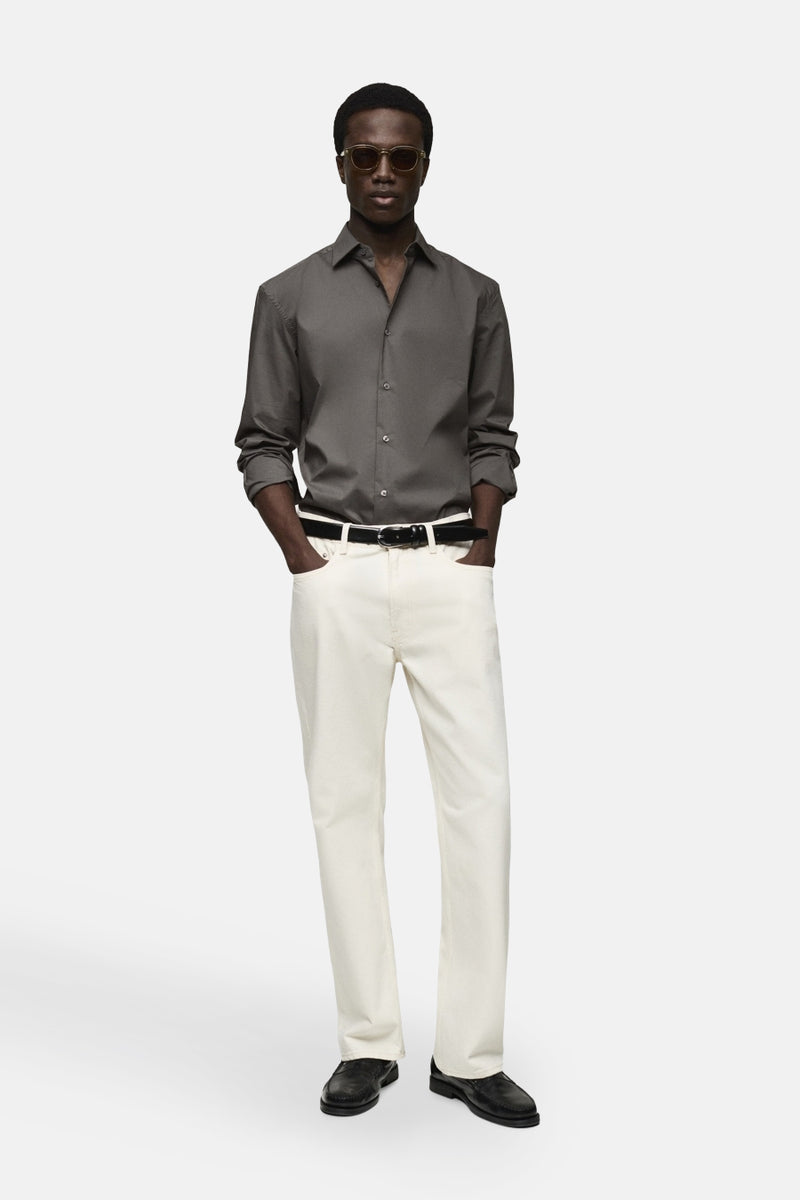 Grijze blouse met lange mouwen van MANGO, gedragen met een lichte broek, een zwarte leren riem en een zonnebril.