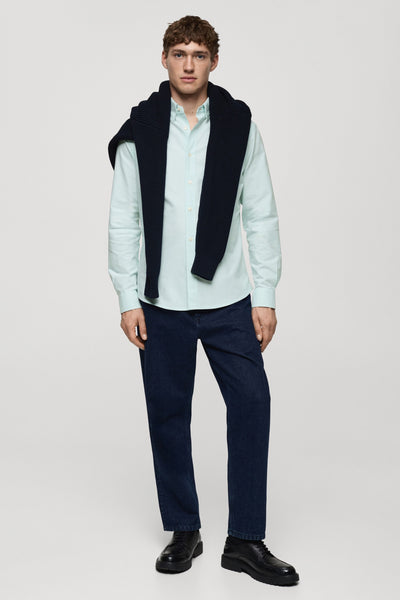Groen overhemd met lange mouwen van MANGO, gedragen met een zwarte trui over de schouders en een donkerblauwe jeans.