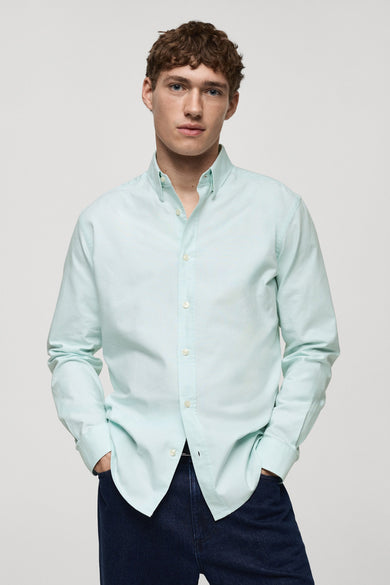 Groen overhemd met lange mouwen van MANGO, gedragen met een marineblauwe broek, handen in de zakken.