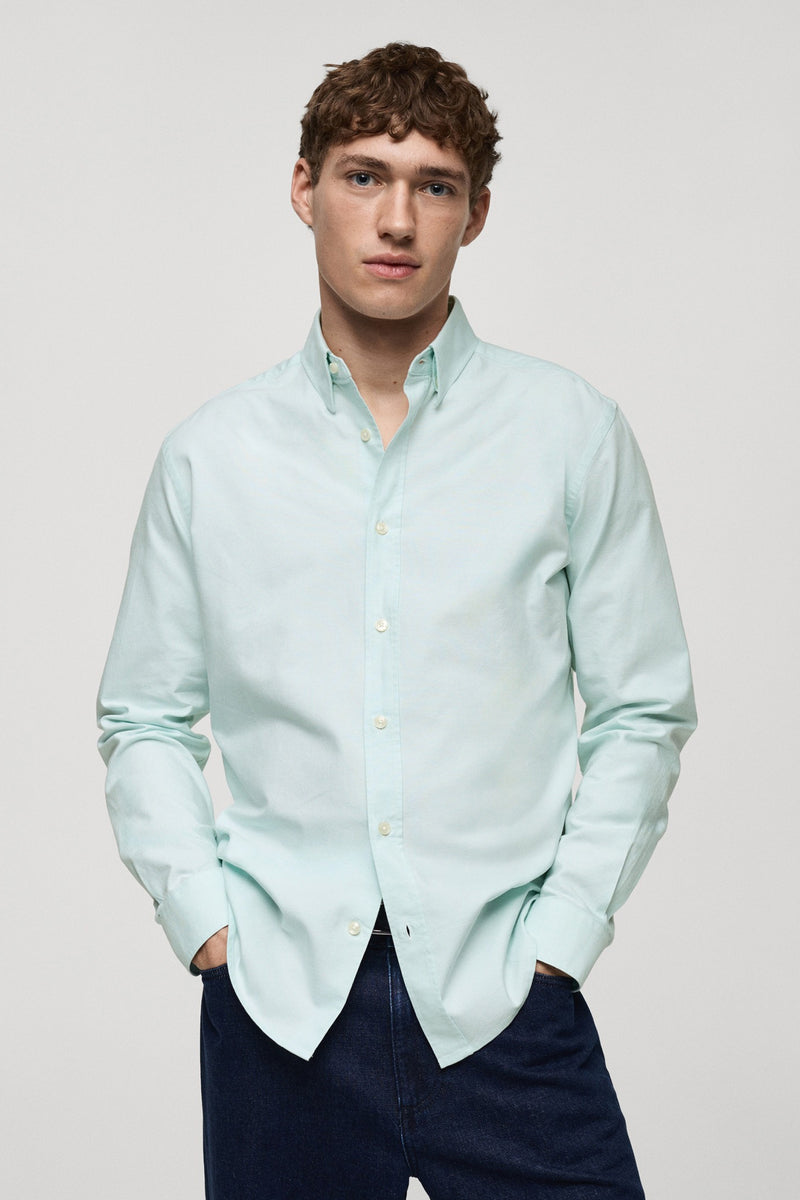 Groen overhemd met lange mouwen van MANGO, gedragen met een marineblauwe broek, handen in de zakken.