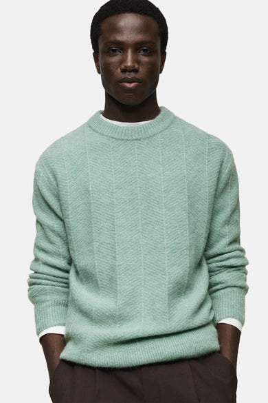 Ronde hals trui blauw van MANGO, chevronpatroon, gedragen met een bruine broek en enkellaarsjes.