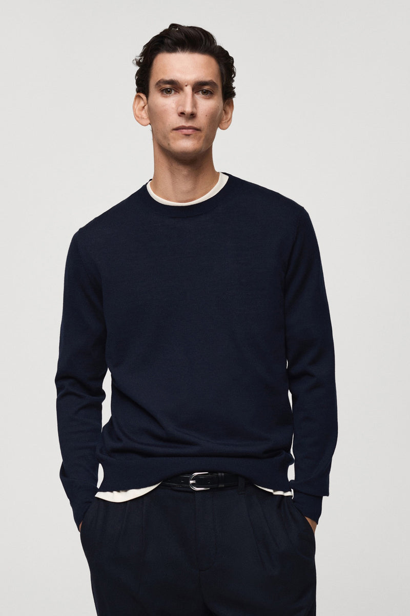 Ronde hals blauwe trui van MANGO, van achteren gezien, gedragen met een marineblauwe broek met klepzakken.
