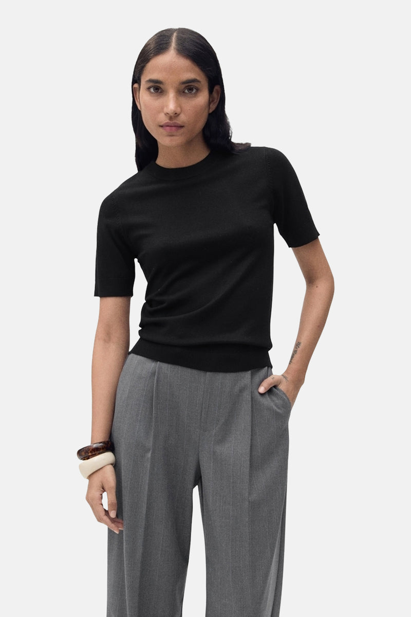 Zwarte rondehals trui van MANGO, gedragen met een grijze gestreepte broek en beige en bruine armbanden.