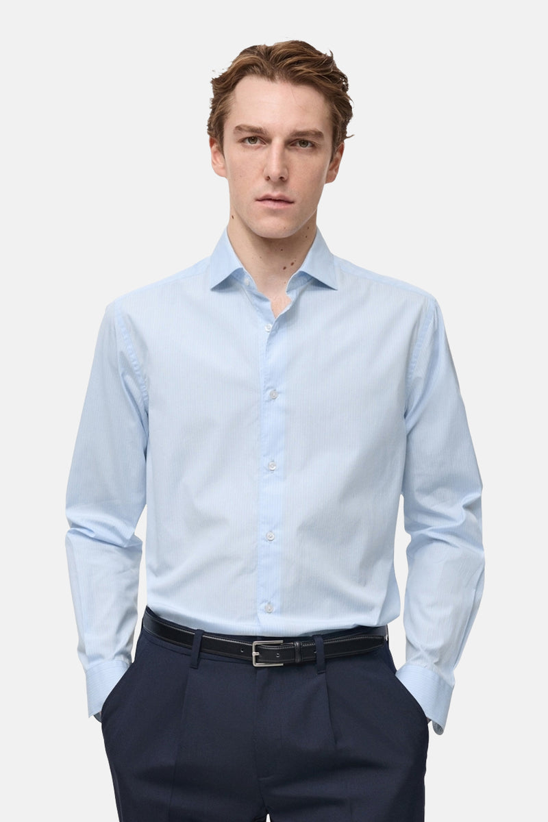 Chemise bleue à manches longues de MANGO, portée avec une ceinture et un pantalon bleu marine.