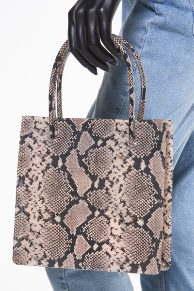 Sac à main beige en cuir synthétique par MANGO, motif serpent, porté par une main de mannequin sur un pantalon en jean bleu clair.
