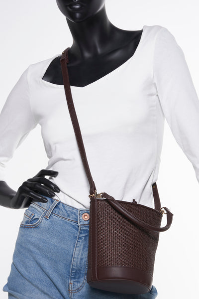Sac à main marron, de MANGO, avec une texture tressée et porté sur un mannequin avec un t-shirt blanc et un jean.
