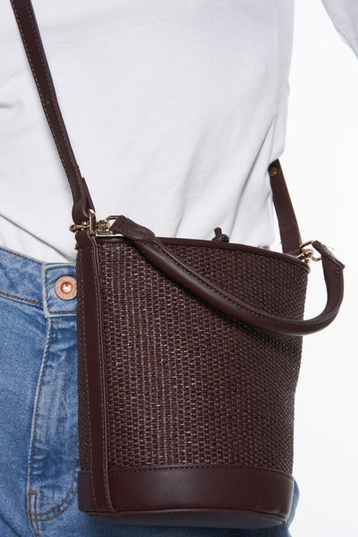 Sac à main tressé brun de MANGO, avec bandoulière réglable, porté avec un t-shirt blanc et un jean bleu.