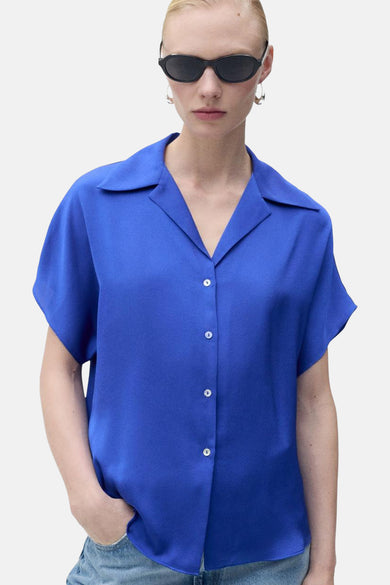 Blauw overhemd met korte mouwen van MANGO, achterkant, met een lichte spijkerbroek en zilveren oorbellen.