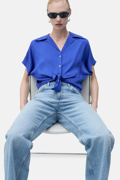 Blauwe blouse met korte mouwen van MANGO, met strik in de taille, gedragen met een wijde jeans en een zonnebril.