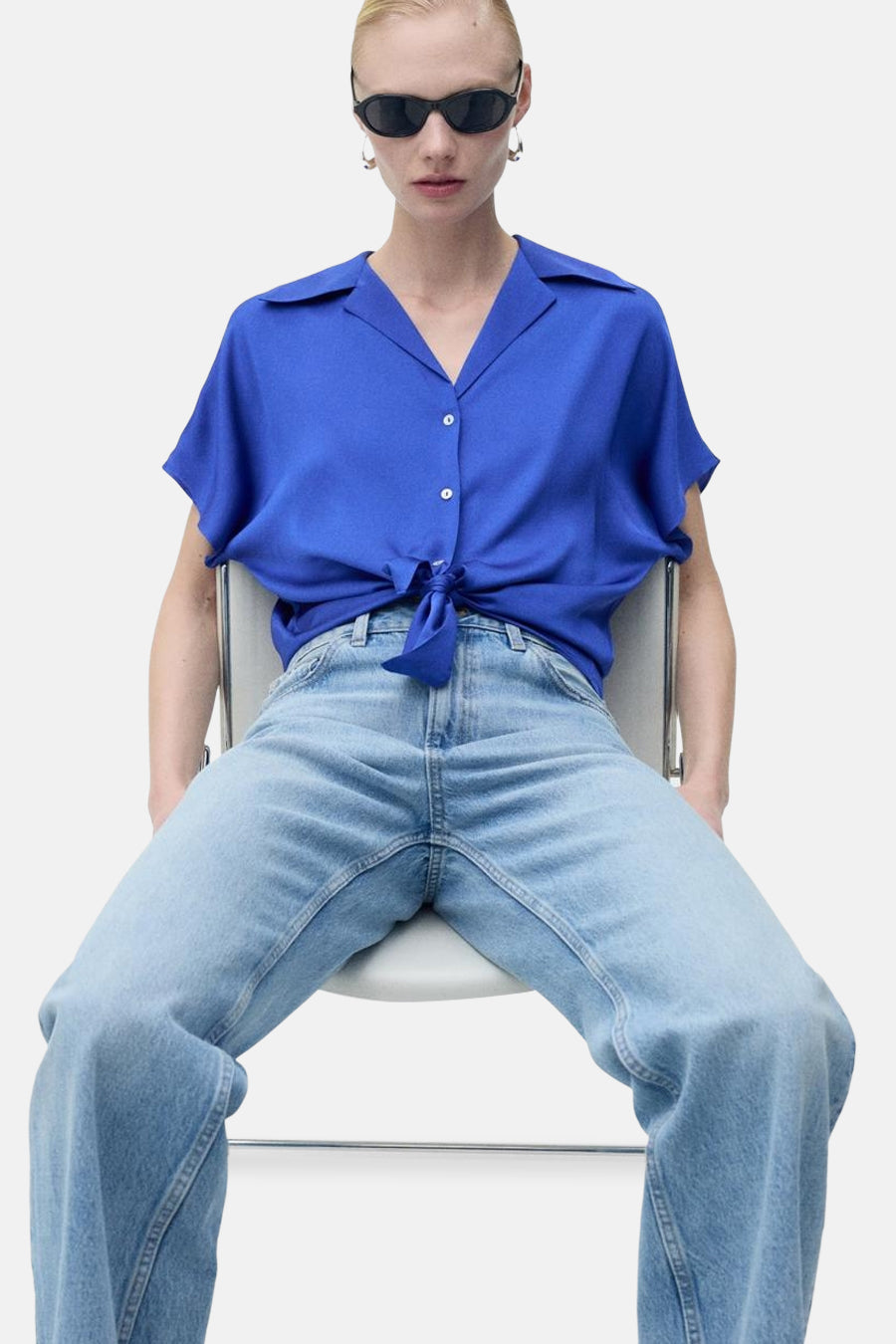 Blauwe blouse met korte mouwen van MANGO, met strik in de taille, gedragen met een wijde jeans en een zonnebril.