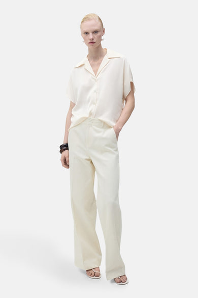 Chemisier écru à manches courtes de MANGO, porté avec un pantalon taille haute et des sandales.