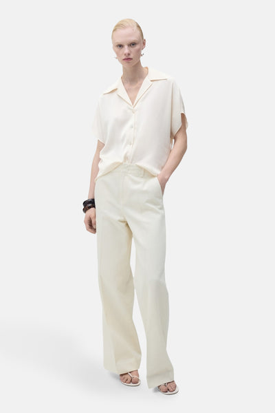 Chemisier écru à manches courtes de MANGO, porté avec un pantalon taille haute et des sandales.