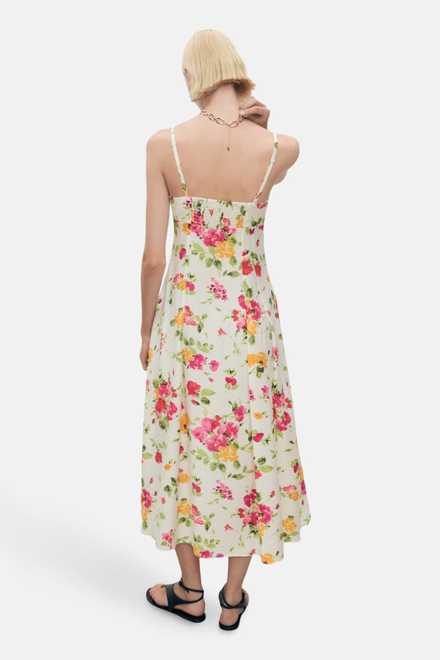 Robe d'été fleurie multicolore de MANGO, avec fines bretelles et dos smocké, portée avec des sandales noires.
