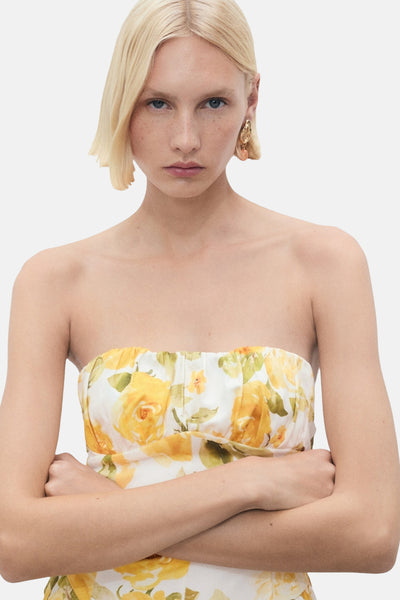 Robe jaune imprimée de roses de MANGO, coupe bustier et bras croisés.
