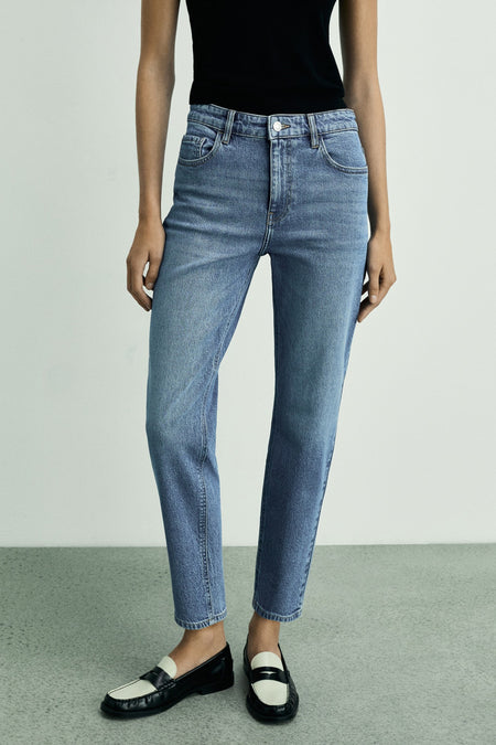 Jean mom en denim bleu moyen de MANGO, porté avec un haut noir et des mocassins bicolores.
