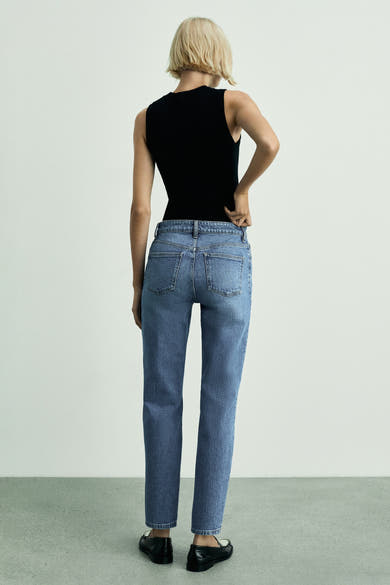 Jeans mom bleu moyen de MANGO, vue de dos, porté avec un débardeur noir et des mocassins noirs.
