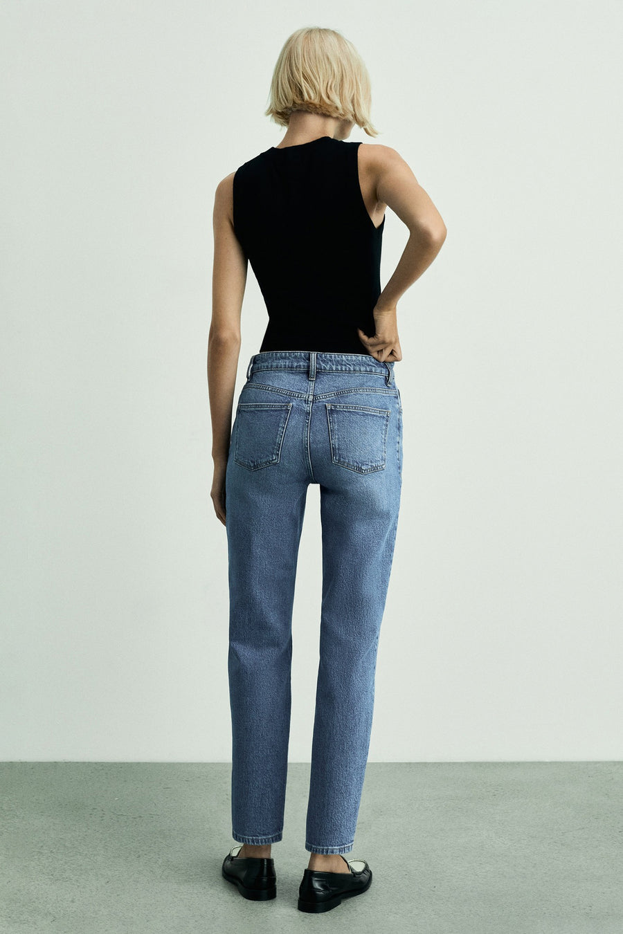 Jeans mom bleu moyen de MANGO, vue de dos, porté avec un débardeur noir et des mocassins noirs.
