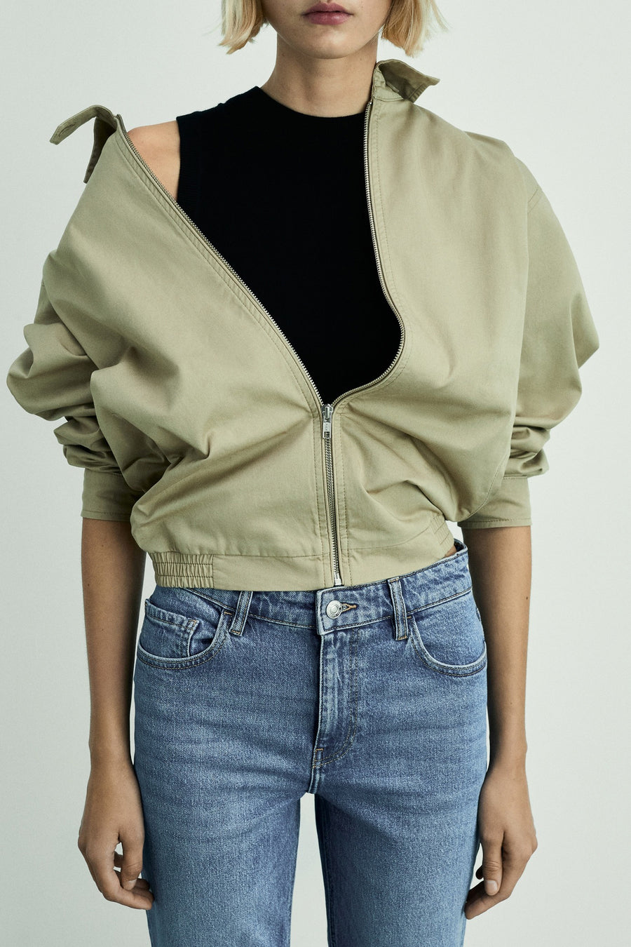 Middelblauwe jeans van MANGO, gedragen met een beige jas met ritssluiting en een zwart topje.
