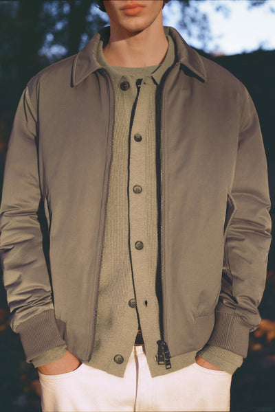 Veste courte marron de MANGO, portée avec un cardigan boutonné et un pantalon blanc, les mains dans les poches.