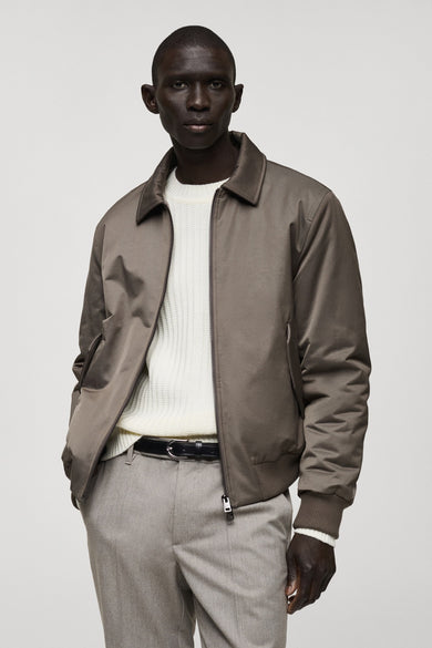 Kort bruin jasje van MANGO, met ritssluiting, gedragen over een gebreide trui en een grijze broek.