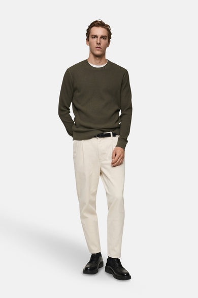 Kaki ronde hals trui van MANGO, gedragen over een wit T-shirt, met een beige broek en zwarte schoenen.
