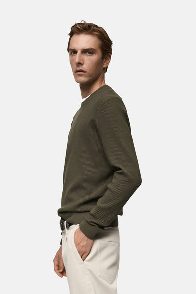 Kaki ronde hals trui van MANGO, met geribbelde textuur, gedragen met een lichte broek en een zwarte riem.