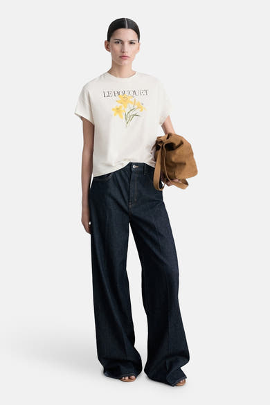 MANGO witte korte mouw T-shirt met bloemprint "Le Bouquet", gedragen met een brede jeans en eenbruroen tas.
