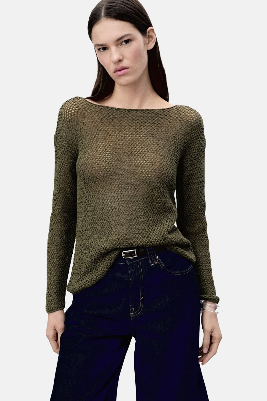 Pull à col rond kaki de MANGO, en maille ajourée transparente, porté avec un jean taille haute ceinturé.