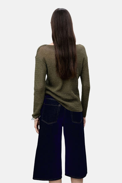 Pull à col rond kaki de MANGO, en maille ajourée, porté avec un pantalon ample bleu marine.
