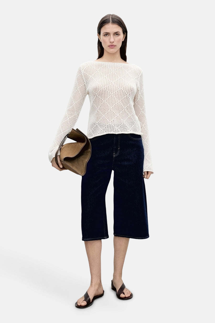 Pull à col rond en maille ajourée écrue de MANGO, porté avec un jean court ample et des sandales en cuir.