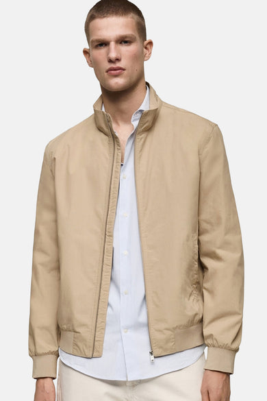Korte beige jas van MANGO, van achteren gezien, met een crèmekleurige broek en zwarte schoenen.