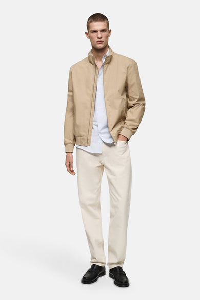 Korte beige jas van MANGO, gedragen met een lichtblauw overhemd en een crèmekleurige broek.