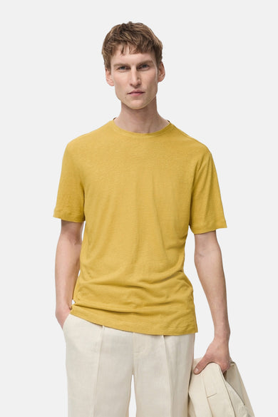 T-shirt à manches courtes jaune de MANGO, porté avec un pantalon en lin écru et une veste assortie tenue à la main.