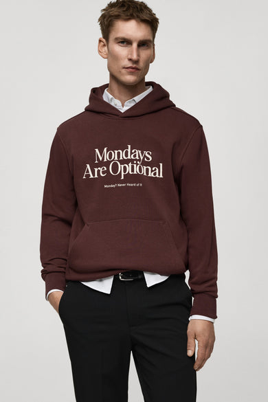 Sweat-shirt bordeaux de MANGO, avec capuche et message blanc, porté avec une chemise blanche et un pantalon noir.
