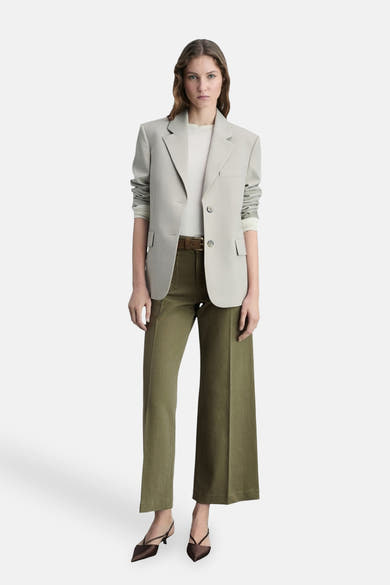 Kaki kleurige broek van MANGO, gedragen met een bruine riem, een gebroken wit T-shirt en een lichtgrijs blazer.