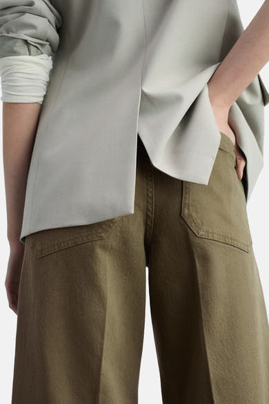 Kaki broek van MANGO, wijde pasvorm met zichtbare achterzakken, gedragen met een grijze blazer.