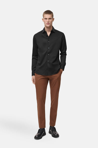 Chemise noire à manches longues de MANGO, portée avec un pantalon marron et des chaussures noires.