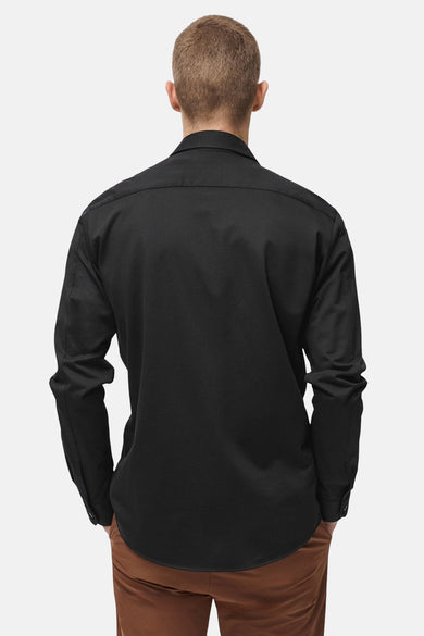 Chemise noire à manches longues de MANGO, vue de dos, portée avec un pantalon marron.