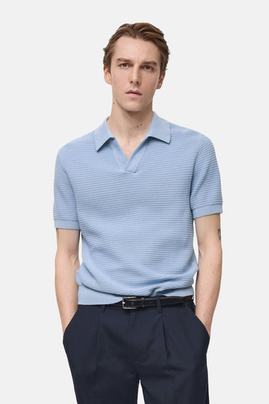 Polo bleu à manches courtes de MANGO, en maille texturée, porté avec un pantalon marine à ceinture noire.
