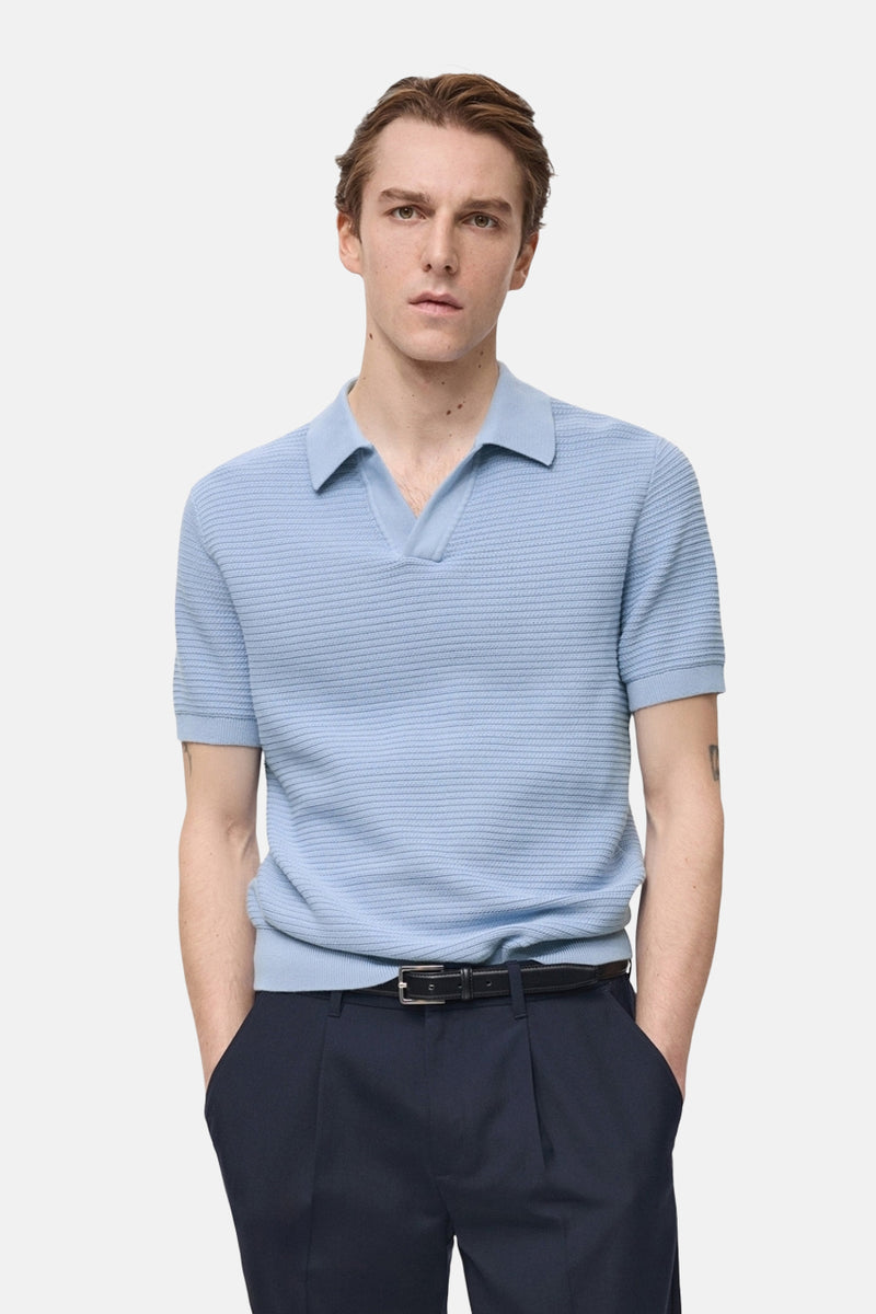 Polo bleu à manches courtes de MANGO, en maille texturée, porté avec un pantalon marine à ceinture noire.
